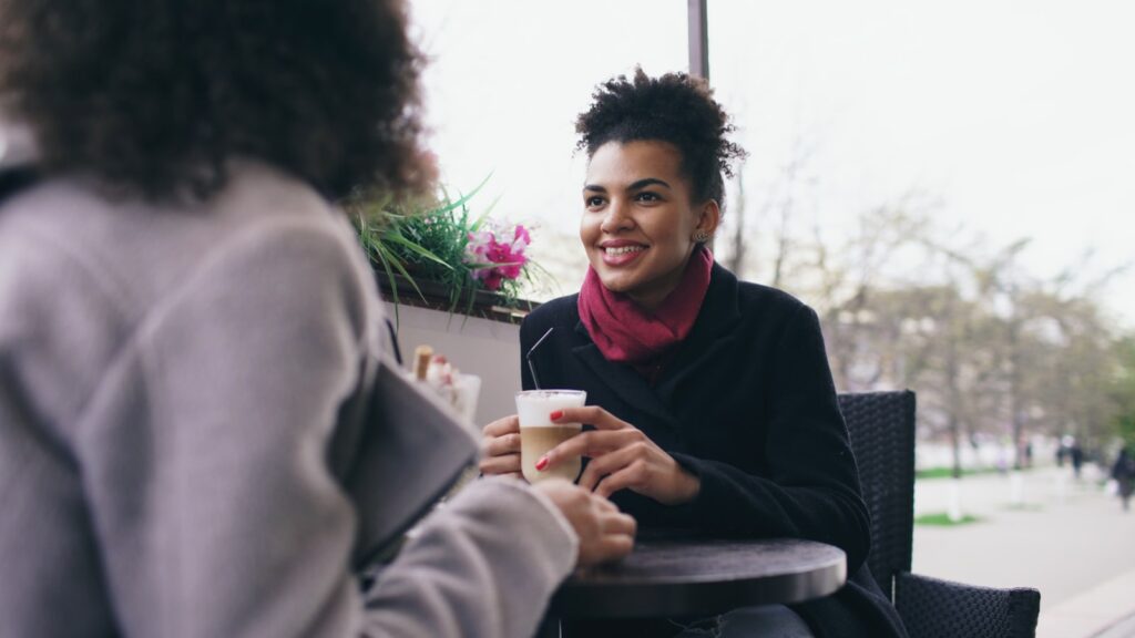 Two women talking at a cafe with coffee.