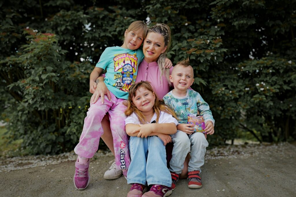 A woman poses with three smiling children outdoors.
